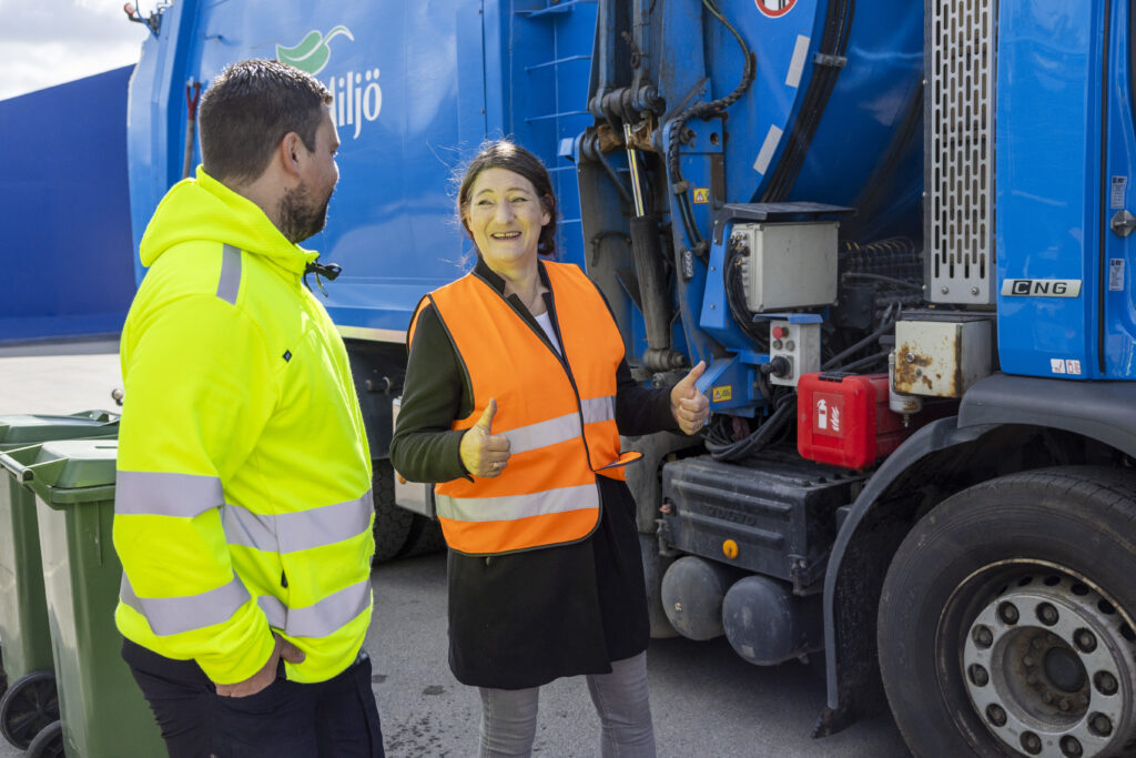 Man och kvinna i varselväst står framför sopbil.
