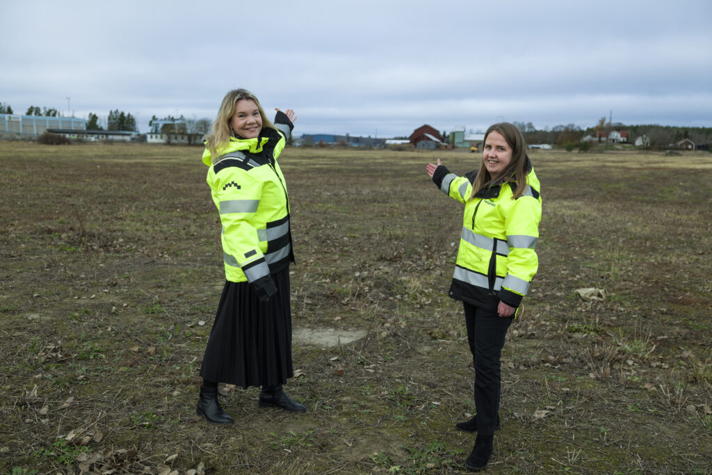 Två personer i varselkläder står på ett fält